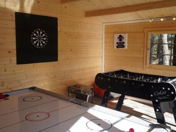 Una habitación con paredes de madera, un dardo y una mesa de fútbol de mesa, y una ventana con vistas a árboles.