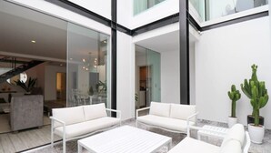 Un espace de vie extérieur moderne, avec des meubles blancs, notamment des canapés et une table basse, ainsi que deux cactus en pot.