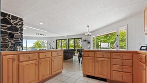 Une cuisine spacieuse avec des meubles en bois, un mur d’accent en pierre, de grandes fenêtres et une vue sur l’extérieur.