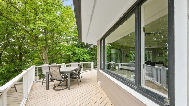 Une terrasse en bois avec une table et des chaises, de grandes fenêtres et une vue sur les arbres.