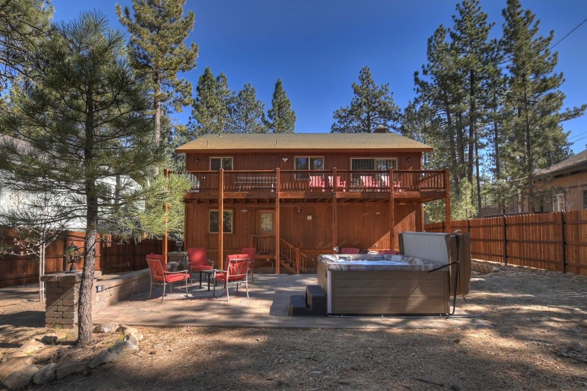 A two-story wooden cabin with a hot tub, outdoor seating, and a fenced yard.