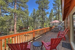 A wooden deck with red chairs and a table, overlooking a forested area.