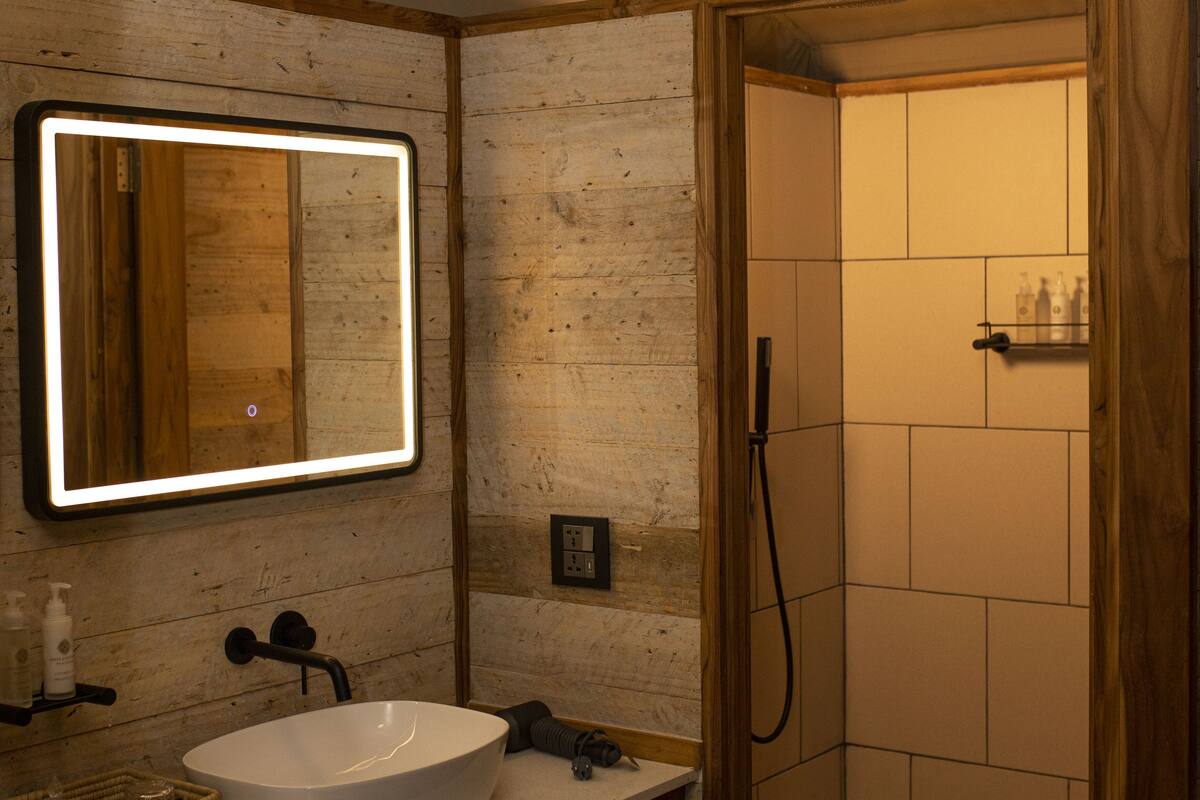 A bathroom with a white sink, a mirror with a light, and a shower area.