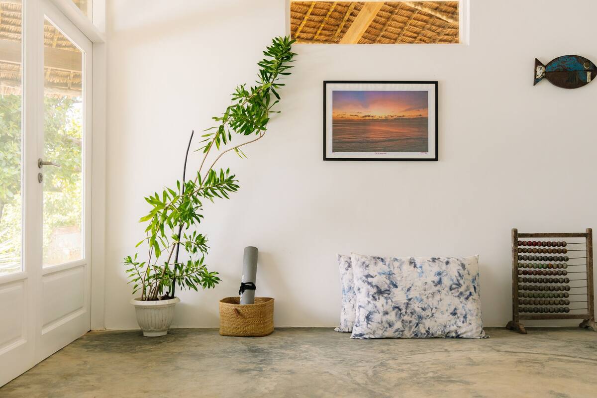 A room with a concrete floor, a potted plant, a framed picture, a pillow, and a wooden abacus.