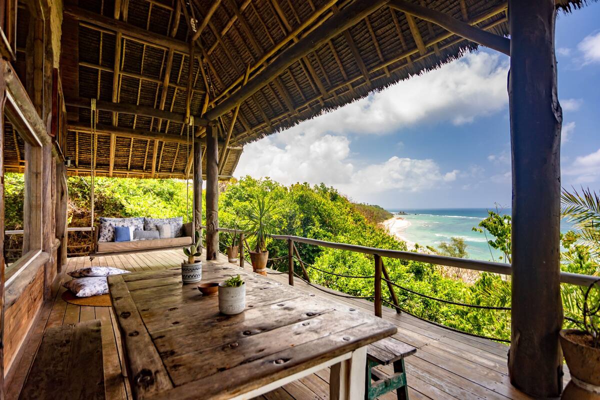 A wooden deck with a thatched roof overlooking a beach and ocean.