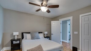 Ein Schlafzimmer mit Bett, Nachttischen, Deckenventilator und einer Tür zu einem anderen Raum.
