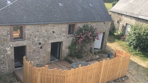Ein Haus aus Stein mit einer Holzterrasse und einem eingezäunten Garten.