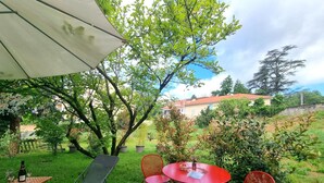 Une terrasse extérieure avec une table et des chaises, une bouteille de vin et un grand parasol.