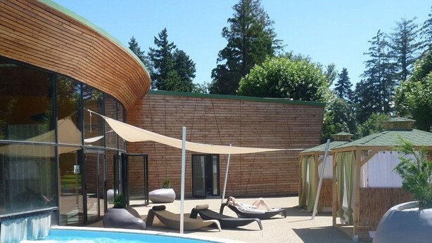 Un espace piscine extérieur moderne, avec des chaises longues et un bâtiment en bois en arrière-plan.