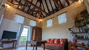 A rustic room with exposed wooden beams, a television, a sofa, and a bookshelf. - Charming Cottage with WiFi and Pets Allowed (Saint-Romain)