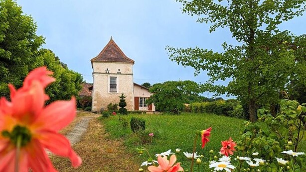A stone tower house with a red roof, surrounded by a lush garden with various flowers and trees. - Charming Cottage with WiFi and Pets Allowed (Saint-Romain)
