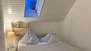 Un dormitorio con tragaluz, una mesita de noche con lámpara y una pequeña estantería con una planta.