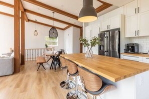 A modern kitchen with wooden beams, a central island with bar stools, stainless steel appliances, and a hanging pendant light.