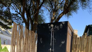 Una ducha exterior de madera con una pared negra, rodeada por un cerco de madera y un banco de piedra.