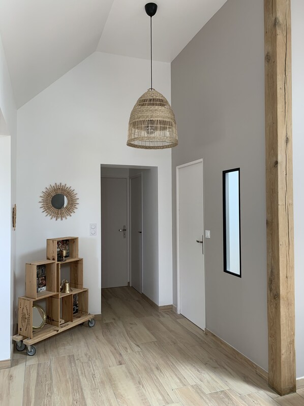 A hallway with a wooden floor, a wicker pendant light, a sunburst mirror, and a wooden shelf with decorative items. - Maison Ty Ruz à 120m de la Plage (Plounéour-Brignogan-plages)