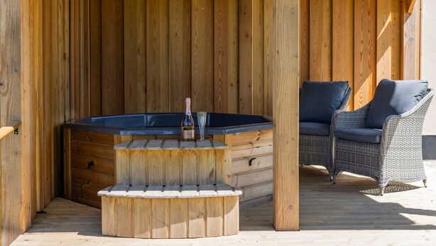 Una terraza de madera con un jacuzzi, una silla de mimbre y un banco de madera.