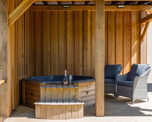 A wooden deck with a hot tub, a wicker chair, and a wooden bench.