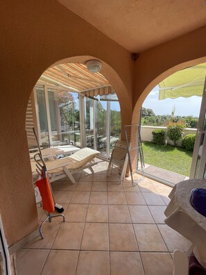 A sunlit patio area with a glass enclosure, a metal chair, and a table. - Exclusive Apartment Sun and Sea  (Novalja)