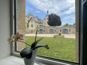 A view of a courtyard with a building in the background, a window with a potted plant, and a stone wall.
