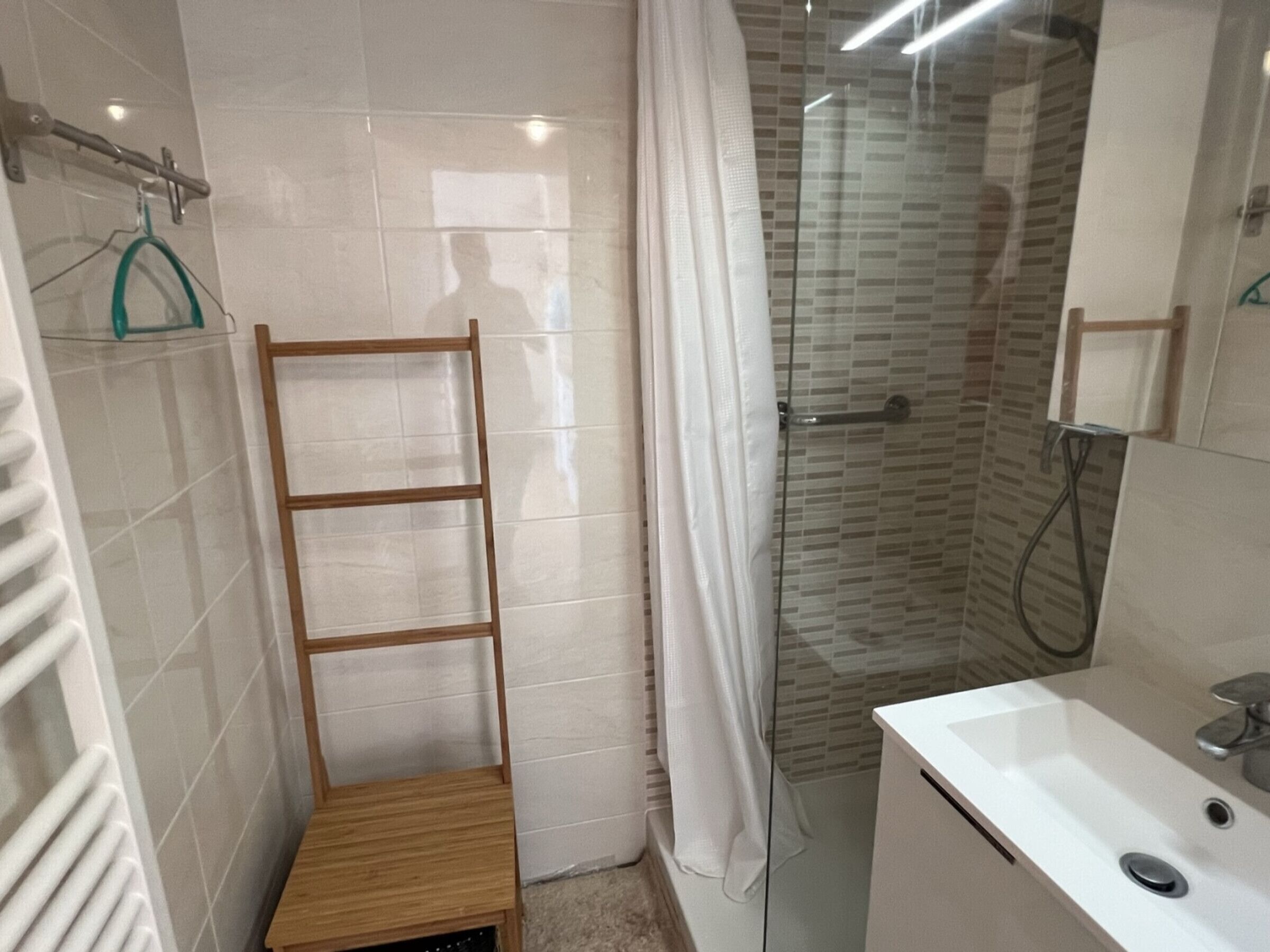 Un baño con ducha, lavamanos y estante de madera.
