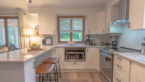 A modern kitchen with white cabinets, a built-in oven, a microwave, and a large window with blinds.
