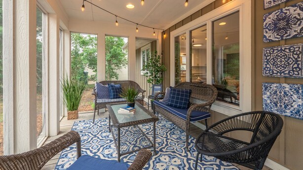 A covered patio area with wicker furniture, a glass table, and decorative lighting.