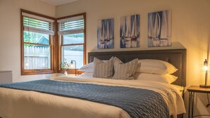 A neatly made bed with a blue quilt, a bedside table with a lamp, and three sailboat paintings on the wall.