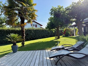 Una terraza de madera con sillones de descanso, una planta en maceta y un césped bien cuidado.