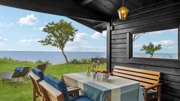 A wooden cabin with a table and chairs, a bench, and a view of the sea. - Beach front home in Rønne with WiFi (Rønne)