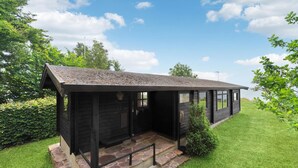 A small, dark wooden cabin with a stone-paved entrance and a grassy lawn. - Beach front home in Rønne with WiFi (Rønne)