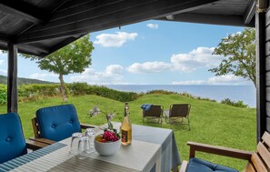 A covered outdoor seating area with a table set for two, a bottle of wine, and a bowl of fruit.