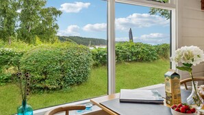 A room with a large window overlooking a garden with a hedge and a distant view of a hill. - Beach front home in Rønne with WiFi (Rønne)