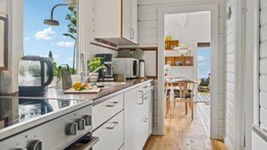 A modern kitchen with white cabinets, a built-in oven, and a view of the beach through the window. - Beach front home in Rønne with WiFi (Rønne)