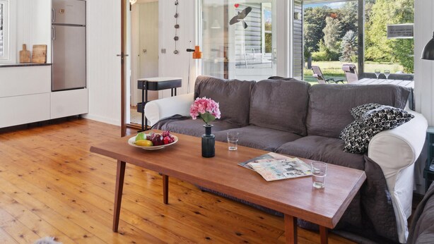 A modern kitchen with white cabinets and a stainless steel refrigerator, a gray sofa with patterned pillows, and a wooden coffee table with a bowl of fruit and a vase of flowers. - 2 bedroom gorgeous home in Askeby (Askeby)