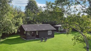 A small, dark-colored house with a sloped roof, a porch with two chairs, and a well-maintained lawn. - 2 bedroom gorgeous home in Askeby (Askeby)