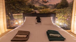 A bedroom with a bed, two pillows, and a view of a mountainous landscape through a window. - Luxury Lodge on Golf Course with Private Hot Tub, Pool & Gym Access (Le Chambon-sur-Lignon)