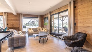 A spacious living area with a sofa, armchairs, and a coffee table. There is a dining table with chairs, and large windows provide natural light and views of the outdoors. - Luxury Lodge on Golf Course with Private Hot Tub, Pool & Gym Access (Le Chambon-sur-Lignon)