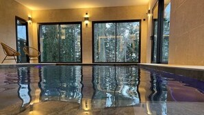 An indoor swimming pool with a clear view of trees outside through large glass doors. - Luxury Lodge on Golf Course with Private Hot Tub, Pool & Gym Access (Le Chambon-sur-Lignon)