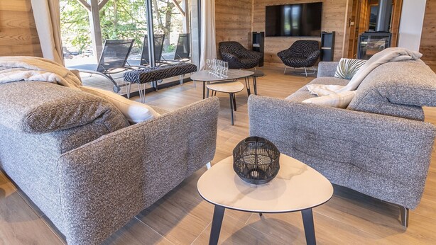 A modern living room with a sofa, two armchairs, a coffee table, and a TV. - Luxury Lodge on Golf Course with Private Hot Tub, Pool & Gym Access (Le Chambon-sur-Lignon)