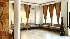 A spacious lobby with a stone accent wall, a large column, and a seating area with a fan. - Laluna Guesthouse (Siem Reap)