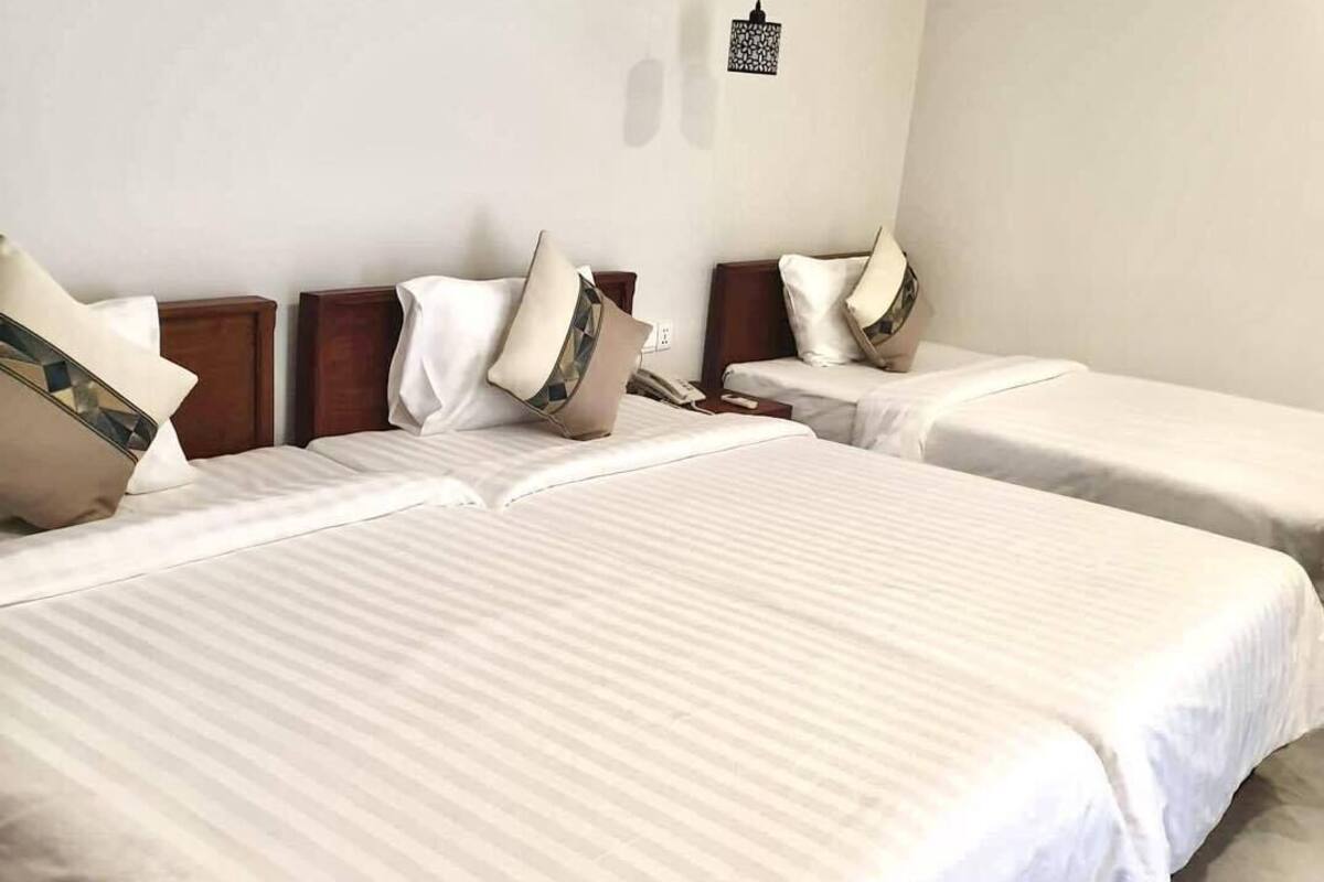 A hotel room with two single beds, a wooden headboard, a hanging light fixture, and a wall-mounted air conditioning unit.