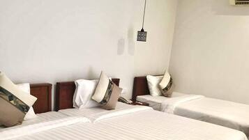 A hotel room with two single beds, a wooden headboard, a hanging light fixture, and a wall-mounted air conditioning unit.