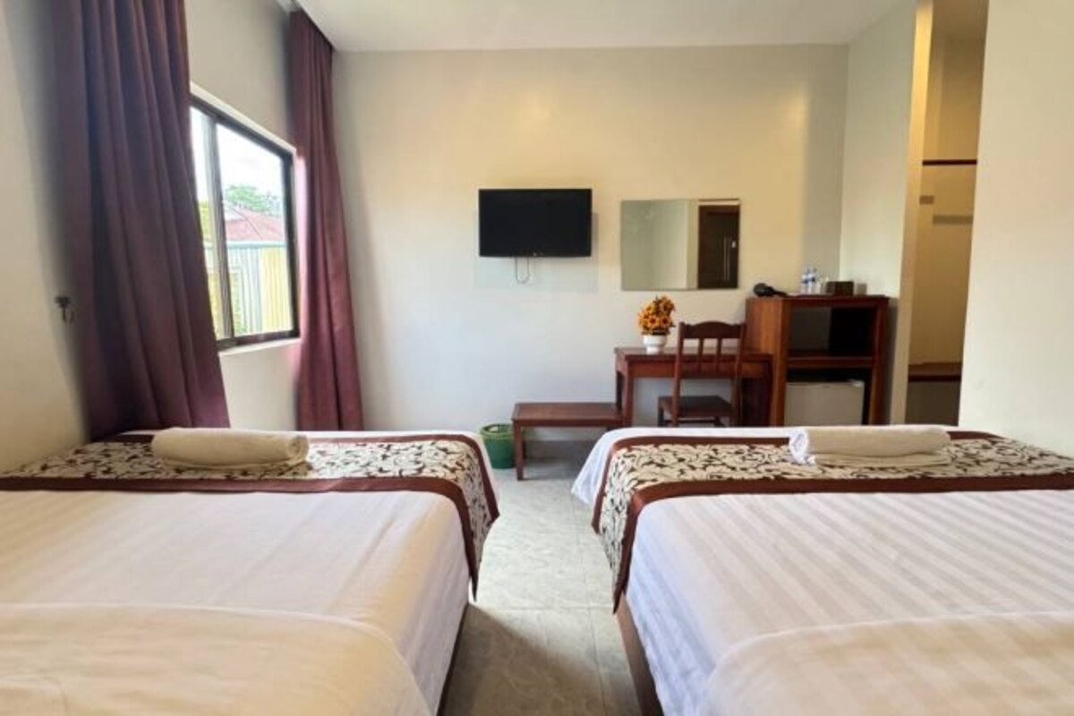 A hotel room with two beds, a desk, a chair, a TV, and a window with curtains.