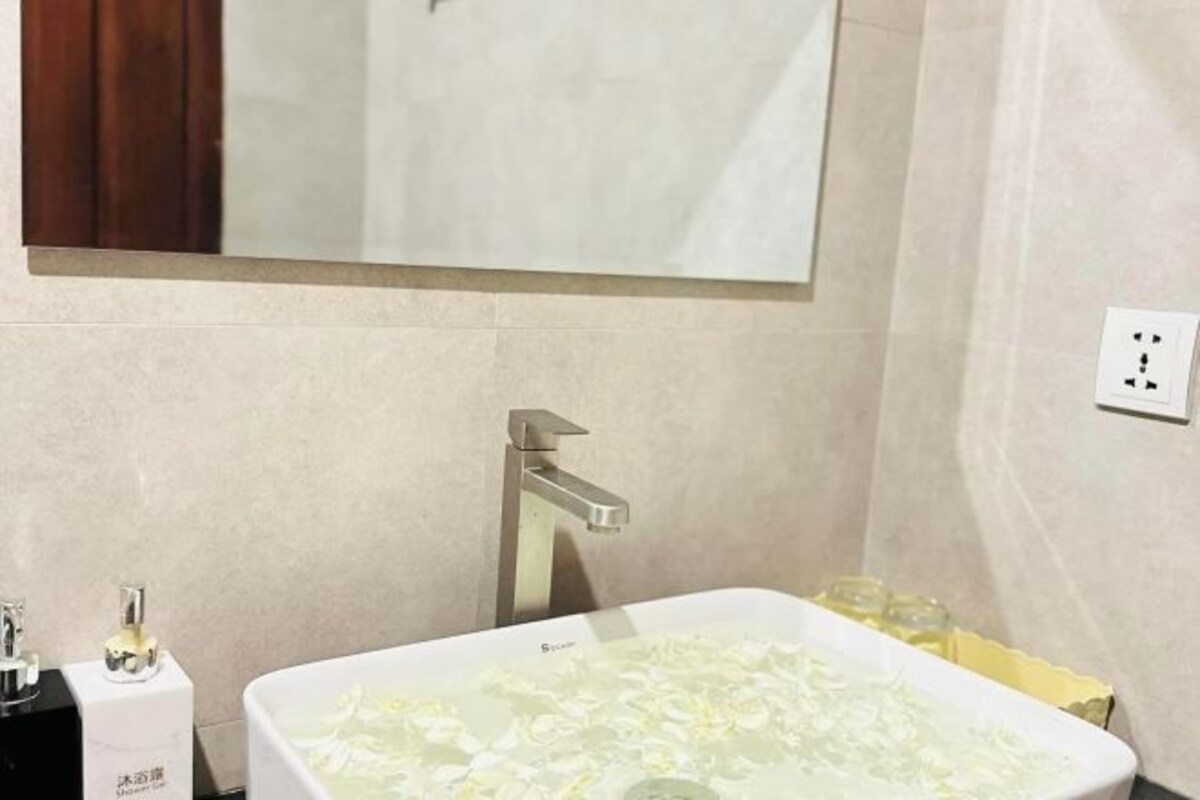 A bathroom with a bathtub filled with water and rose petals, a modern faucet, and a mirror above the tub.