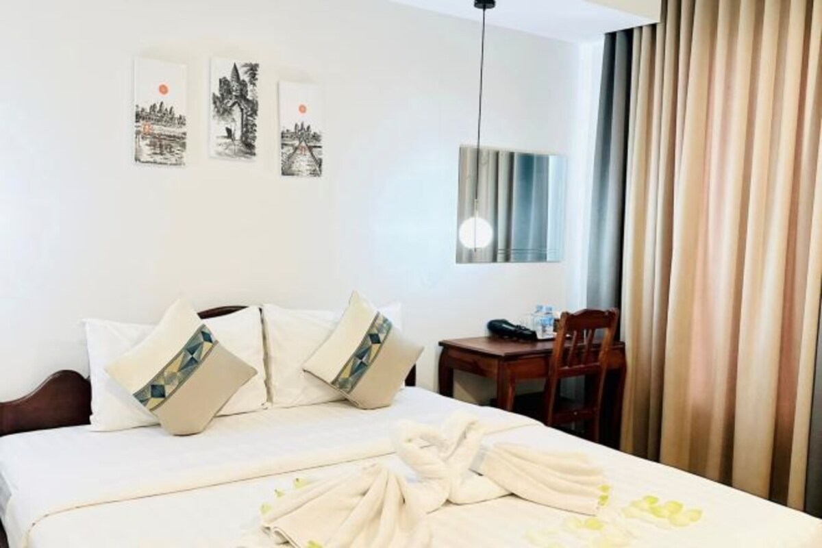 A hotel room with a bed, two pillows, a bedside table, a chair, and a window with curtains.