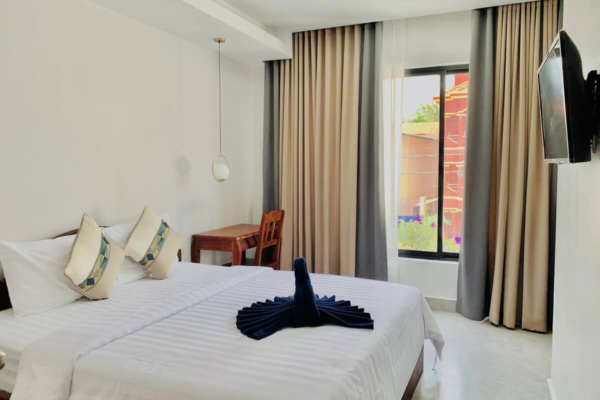 A hotel room with a large bed, a wooden chair, a small table, and a TV mounted on the wall.