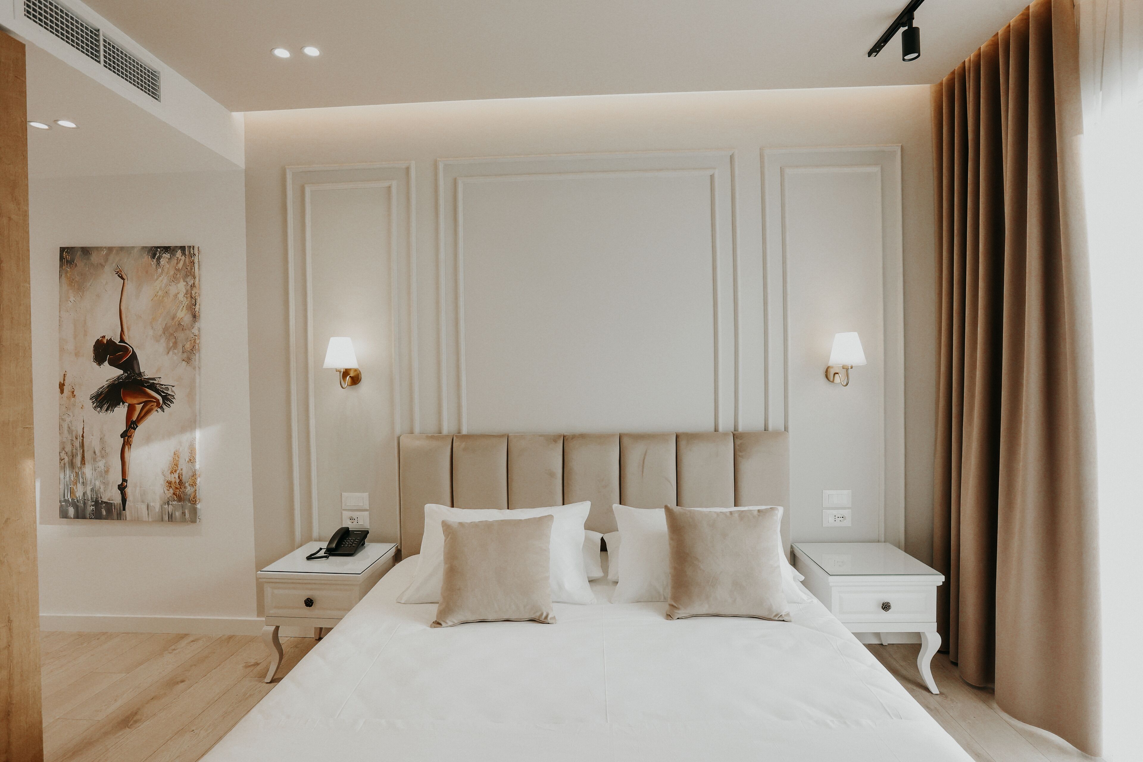 A neatly arranged bedroom with a large bed, bedside tables, and a painting on the wall.