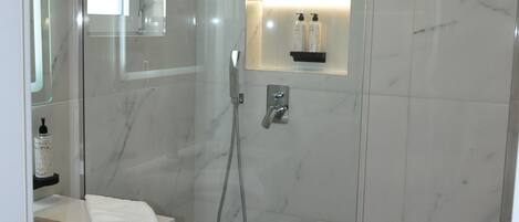 A modern bathroom with a glass-enclosed shower, a vanity with a mirror, and a shelf with toiletries.