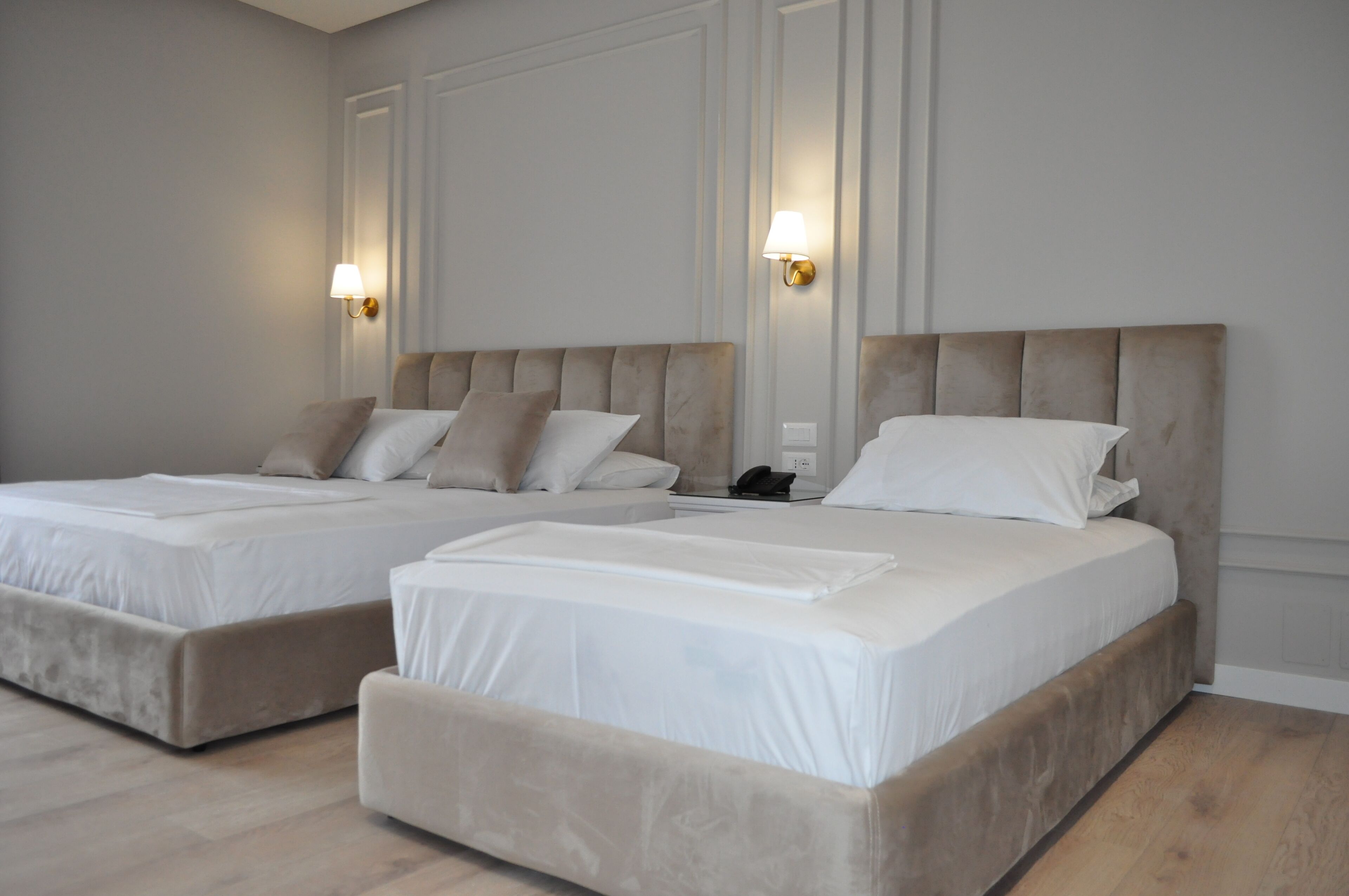 A hotel room with two beds, each with a headboard, white bedding, and wall-mounted lamps.