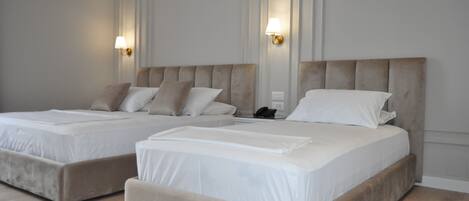 A hotel room with two beds, each with a headboard, white bedding, and wall-mounted lamps.